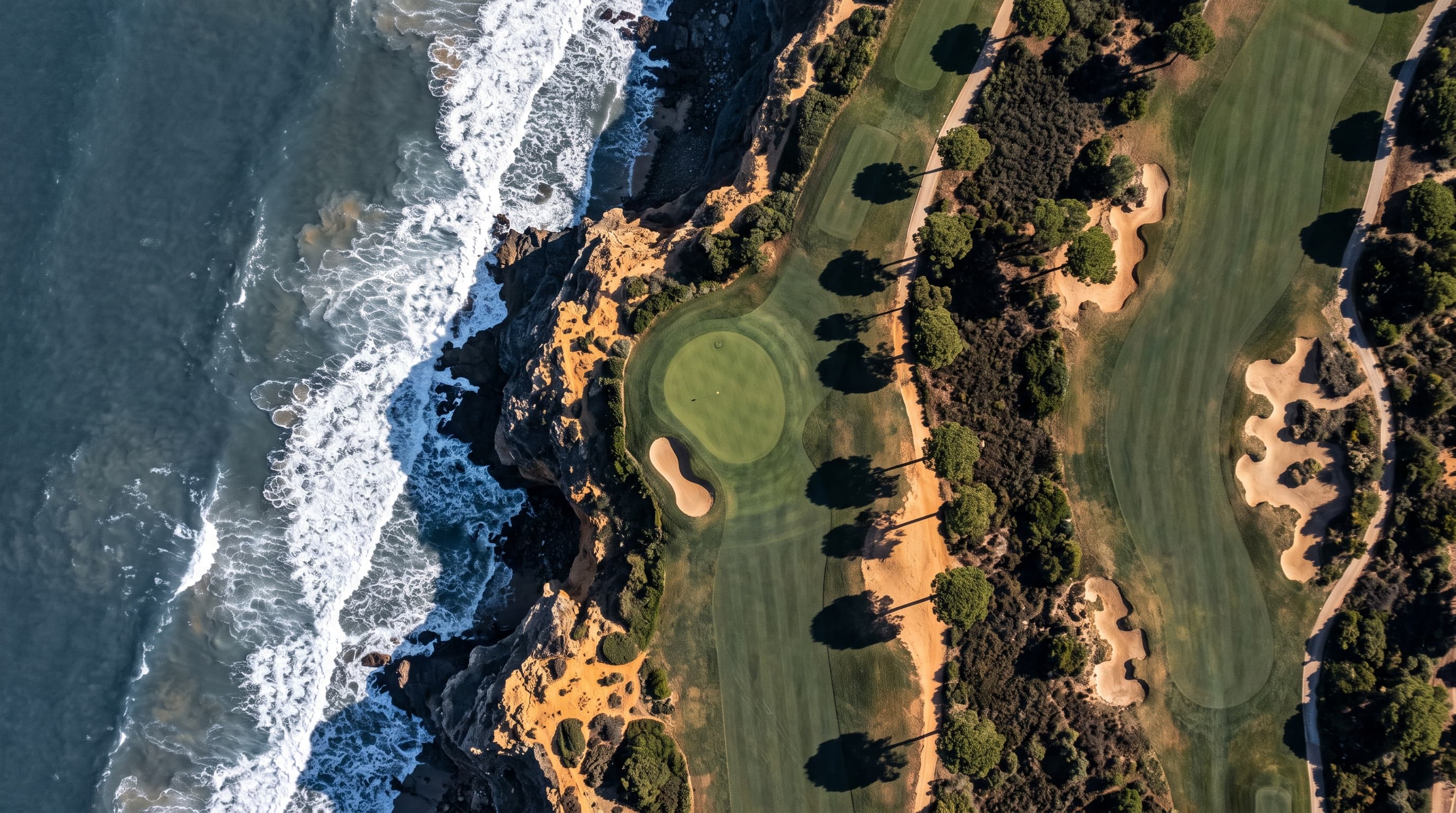 Fairways, bunkers and a green seen from directly above, running along sea cliffs and Atlantic surf